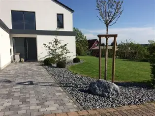 Neuer Garten mit Steinen, Pflanzen und einem kleinen Baum vor einem modernen Haus.